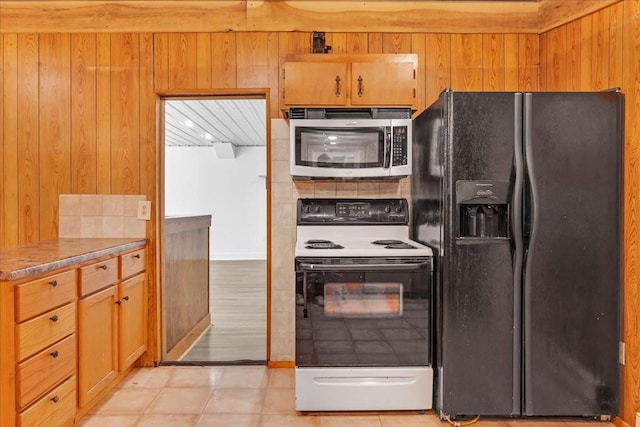 kitchen featuring wooden walls, black refrigerator with ice dispenser, brown cabinetry, stainless steel microwave, and electric stove