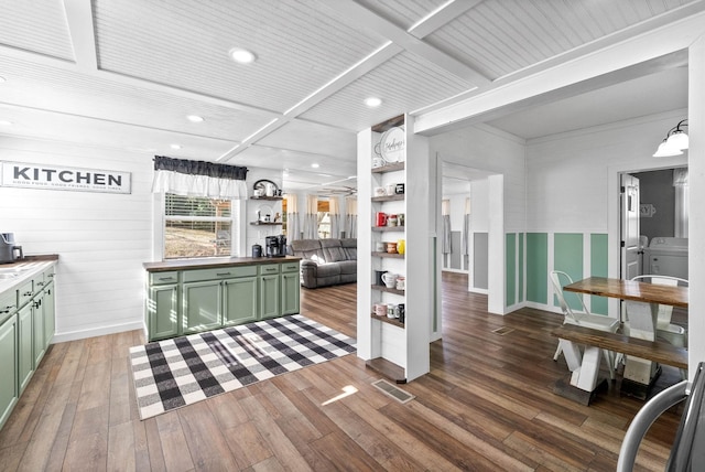 interior space featuring washing machine and clothes dryer, green cabinets, beamed ceiling, wood-type flooring, and visible vents