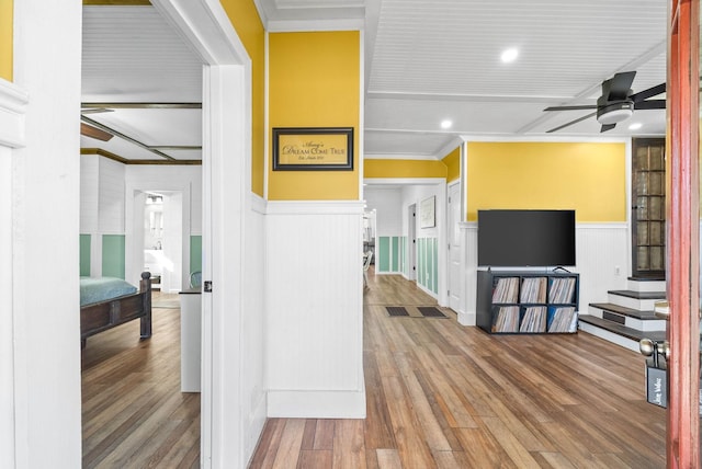 hallway featuring recessed lighting, wood finished floors, ornamental molding, beam ceiling, and wainscoting
