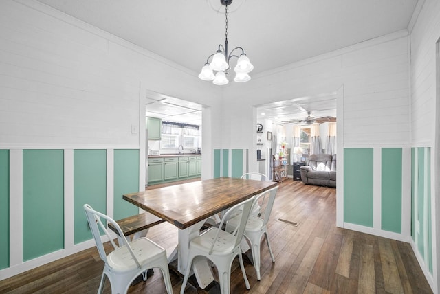 dining space featuring ceiling fan with notable chandelier, hardwood / wood-style flooring, a decorative wall, and crown molding