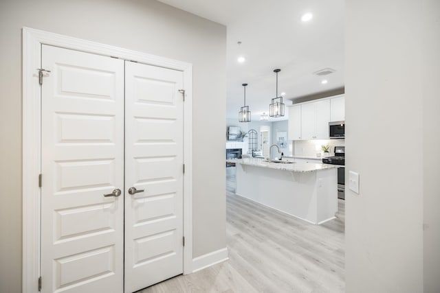 kitchen with a breakfast bar, light stone countertops, stainless steel appliances, white cabinetry, and light wood-style floors