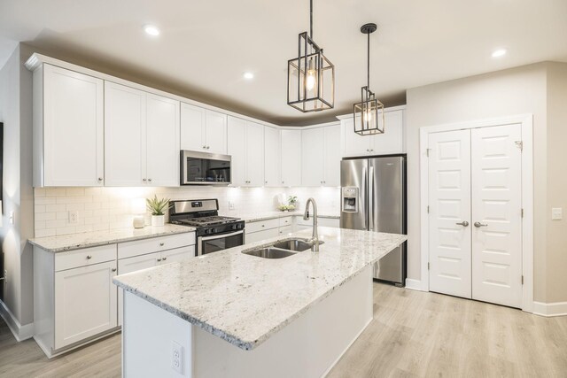 kitchen with a sink, white cabinets, light wood-style floors, and appliances with stainless steel finishes