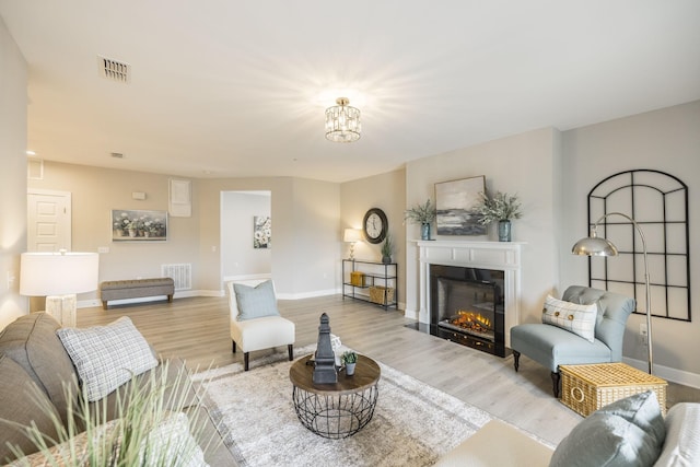 living area featuring visible vents, a glass covered fireplace, and light wood-type flooring