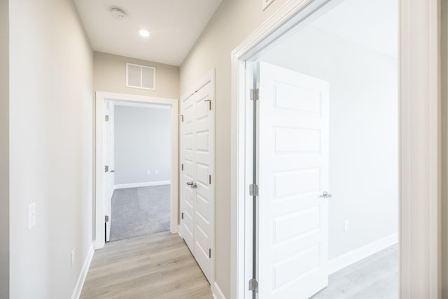 hallway with baseboards, visible vents, and light wood-type flooring
