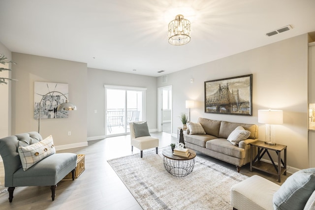 living area featuring baseboards, visible vents, a chandelier, and wood finished floors