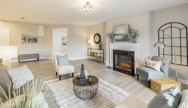 living area with wood finished floors, a glass covered fireplace, baseboards, and visible vents