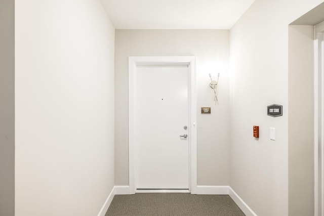 doorway to outside featuring baseboards and dark colored carpet