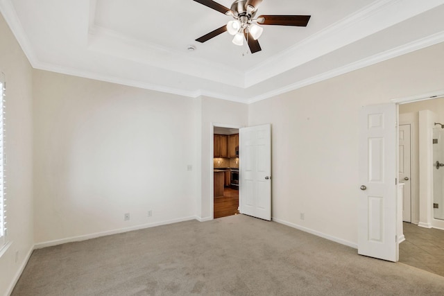 unfurnished bedroom with baseboards, ornamental molding, a ceiling fan, light carpet, and a tray ceiling