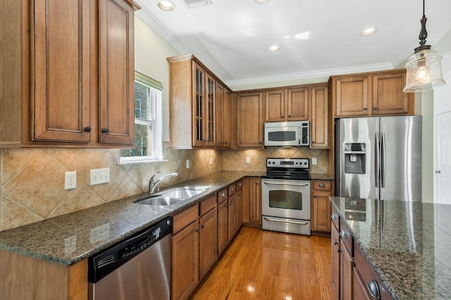 kitchen featuring decorative backsplash, ornamental molding, appliances with stainless steel finishes, a sink, and brown cabinetry