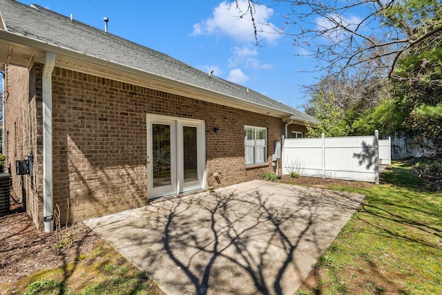 rear view of house featuring fence, a patio area, brick siding, a shingled roof, and a lawn