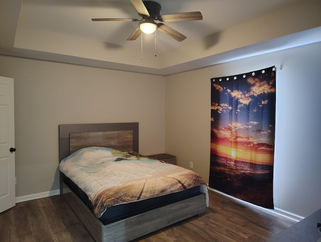 bedroom featuring baseboards, wood finished floors, and a raised ceiling