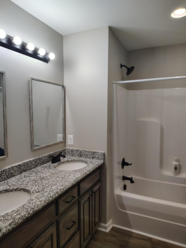 full bath featuring double vanity, a sink, shower / bathtub combination, and wood finished floors