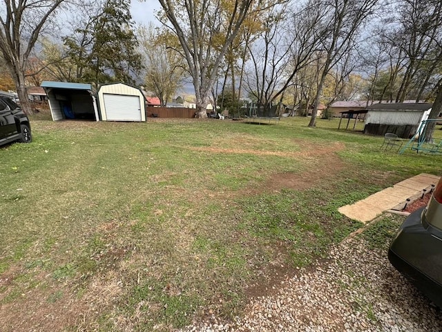 view of yard featuring a trampoline, fence, an outdoor structure, a storage unit, and a garage