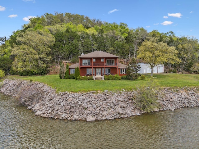 rear view of house featuring a water view, an outdoor structure, a chimney, and a lawn
