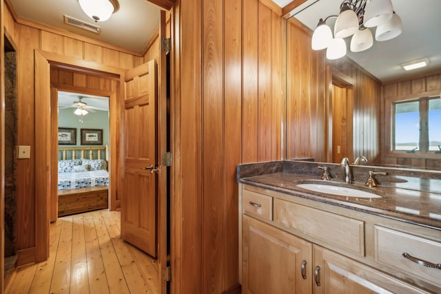 bathroom with vanity, wooden walls, visible vents, hardwood / wood-style floors, and ceiling fan with notable chandelier