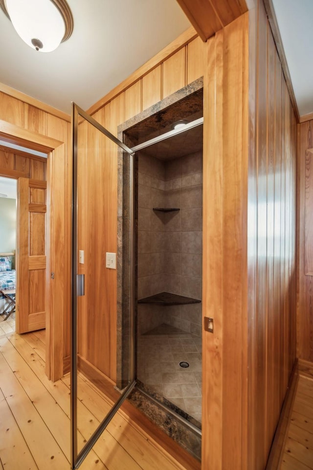 bathroom with wooden walls, wood-type flooring, and a shower stall