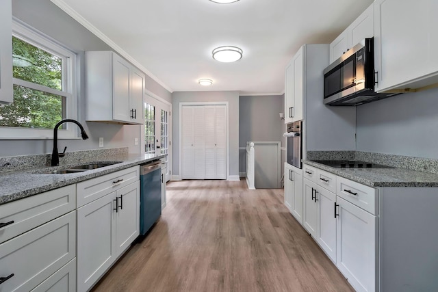 kitchen with crown molding, a sink, white cabinetry, light wood-style flooring, and stainless steel appliances