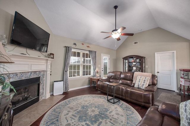 living area featuring vaulted ceiling, a premium fireplace, baseboards, visible vents, and a ceiling fan