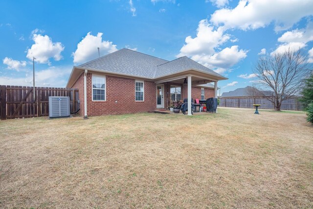 rear view of house featuring a fenced backyard, brick siding, central AC unit, and a lawn