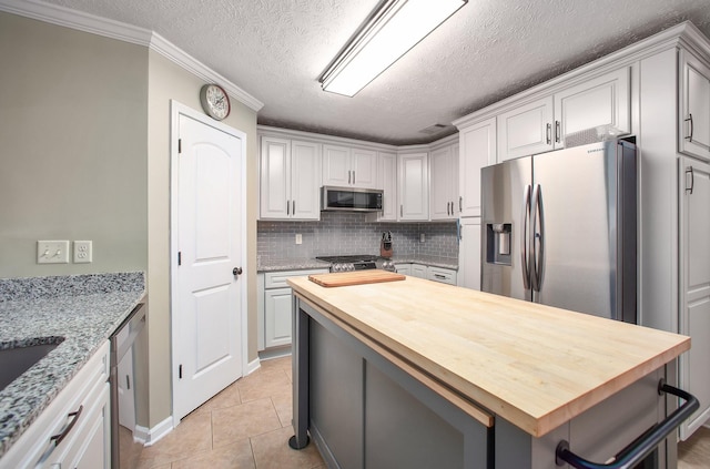 kitchen featuring decorative backsplash, wooden counters, a kitchen island, appliances with stainless steel finishes, and light tile patterned floors