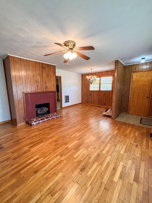 126 Zimmerman St, Hohenwald, TN 38462 - unfurnished living room featuring ceiling fan with notable chandelier, baseboards, wooden walls, light wood finished floors, and a brick fireplace