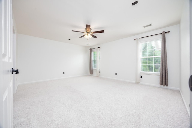 empty room featuring a wealth of natural light, a ceiling fan, light colored carpet, and visible vents