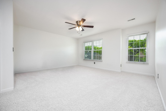 spare room featuring visible vents, a ceiling fan, a healthy amount of sunlight, and light carpet
