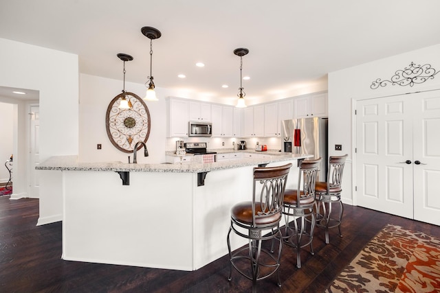 kitchen featuring appliances with stainless steel finishes, a kitchen breakfast bar, light stone countertops, and dark wood-style floors