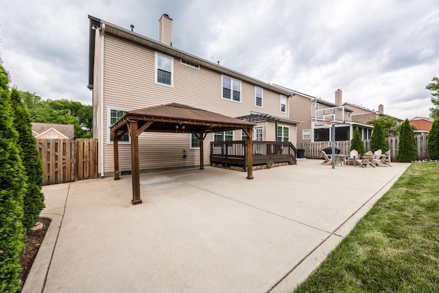 back of property with fence, a wooden deck, a patio, a chimney, and a gazebo