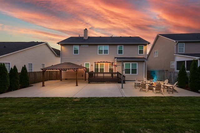 back of house at dusk with fence, a gazebo, a chimney, a patio, and a fire pit