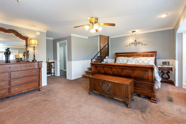 carpeted bedroom featuring a wainscoted wall, a textured ceiling, crown molding, and a ceiling fan