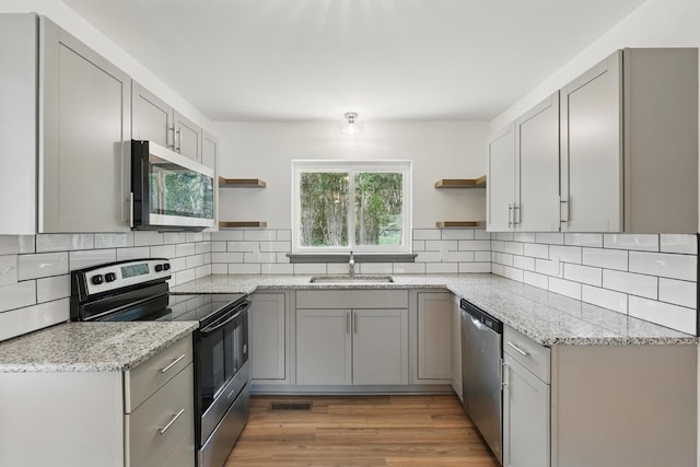 kitchen featuring gray cabinetry, stainless steel appliances, open shelves, and a sink