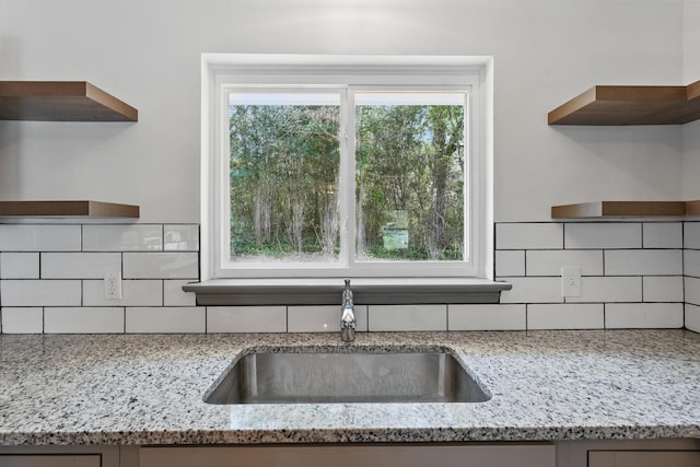 kitchen with tasteful backsplash, open shelves, light stone countertops, and a sink