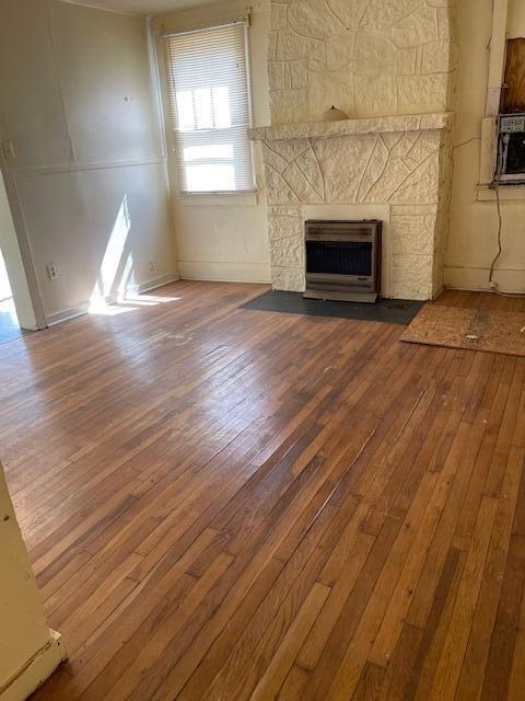 unfurnished living room with heating unit, dark wood-type flooring, and a fireplace