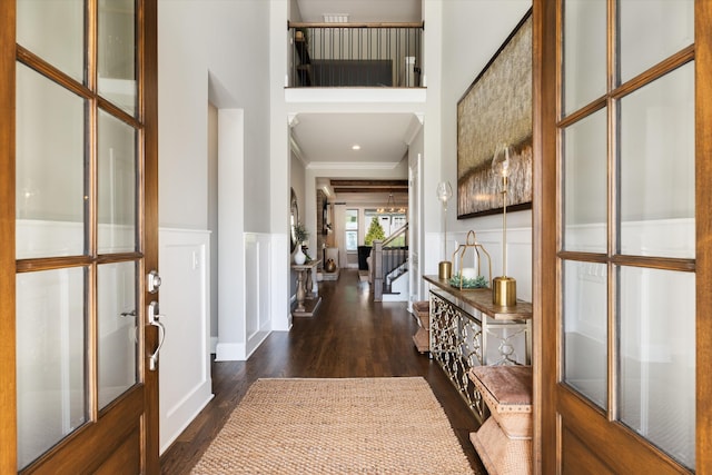 foyer entrance with crown molding, dark wood finished floors, wainscoting, a decorative wall, and a high ceiling