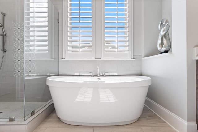 full bathroom featuring a shower stall, a freestanding tub, healthy amount of natural light, and tile walls