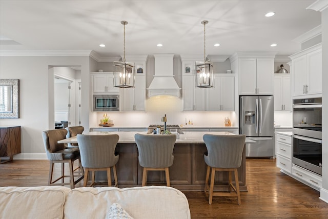 kitchen with appliances with stainless steel finishes, custom range hood, ornamental molding, a kitchen island with sink, and a kitchen bar