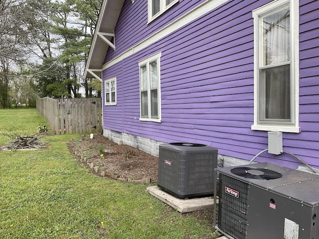 view of side of property featuring central air condition unit, fence, and a lawn