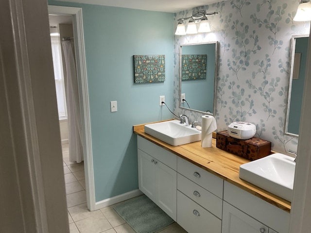 bathroom featuring a sink, tile patterned floors, baseboards, and wallpapered walls