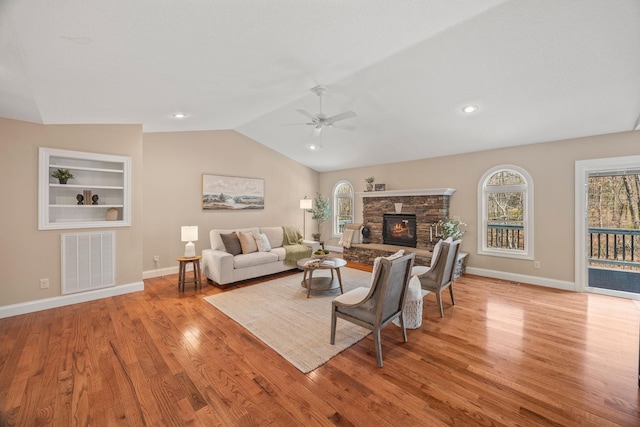 living room featuring a stone fireplace, visible vents, wood finished floors, lofted ceiling, and ceiling fan