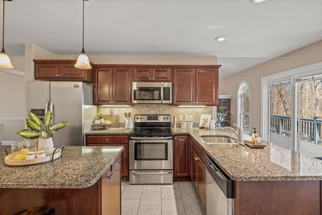 kitchen featuring a peninsula, light stone counters, a sink, stainless steel appliances, and backsplash