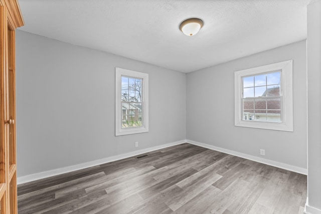 unfurnished room featuring baseboards, a textured ceiling, visible vents, and wood finished floors