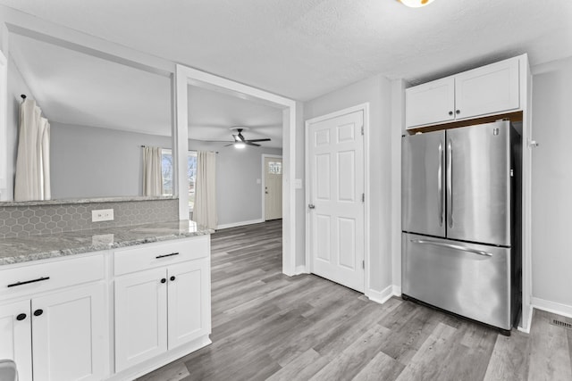 kitchen featuring light wood finished floors, white cabinets, light stone counters, and freestanding refrigerator