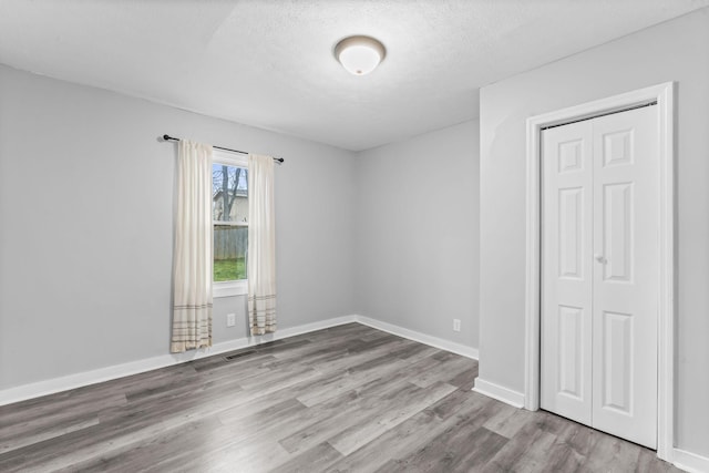 unfurnished room featuring baseboards, visible vents, a textured ceiling, and wood finished floors