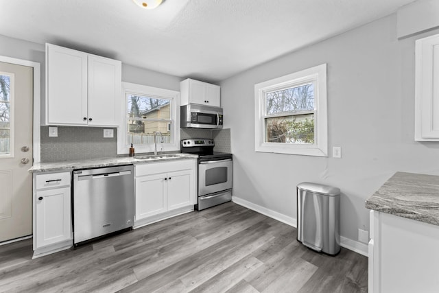 kitchen featuring a wealth of natural light, a sink, backsplash, appliances with stainless steel finishes, and white cabinets