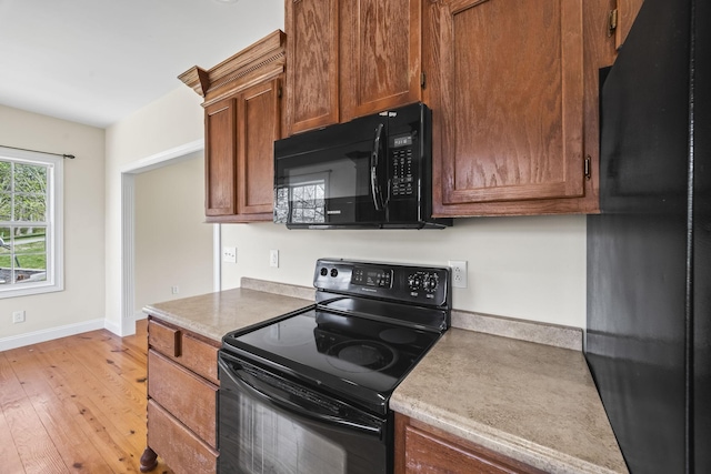 kitchen with light wood-style floors, baseboards, black appliances, and brown cabinets