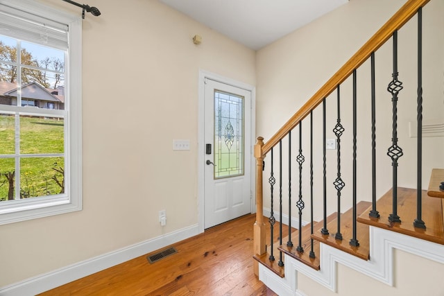 foyer entrance featuring baseboards, visible vents, wood finished floors, and stairway