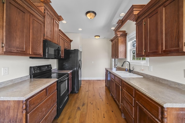 kitchen featuring recessed lighting, baseboards, a sink, light wood finished floors, and black appliances