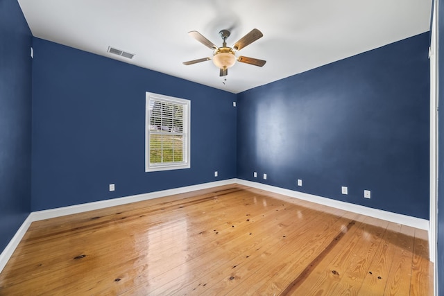 empty room with hardwood / wood-style floors, baseboards, visible vents, and a ceiling fan