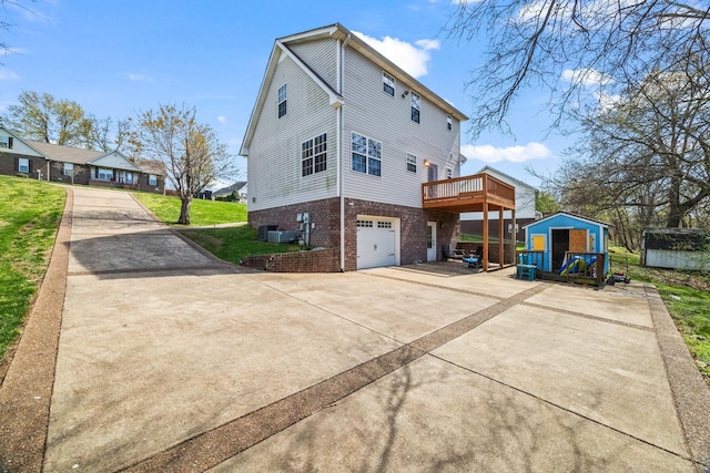 view of side of property featuring an outdoor structure, an attached garage, driveway, a deck, and brick siding